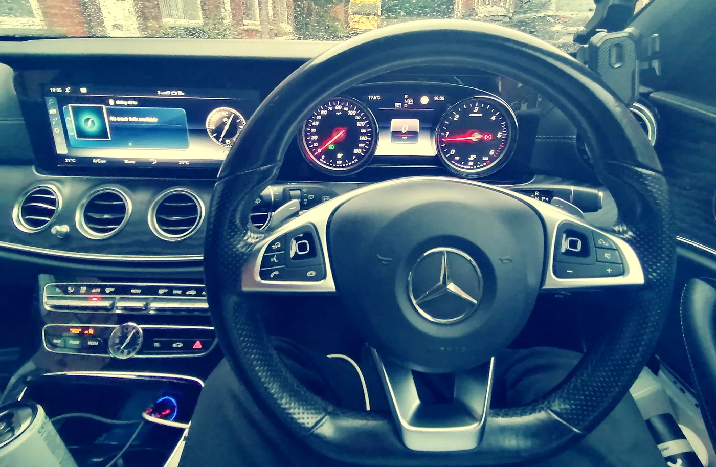 Driver's view of the Mercedes-Benz E-Class cockpit in an MCR Elite Transfers car, showing the instrument display and centre console